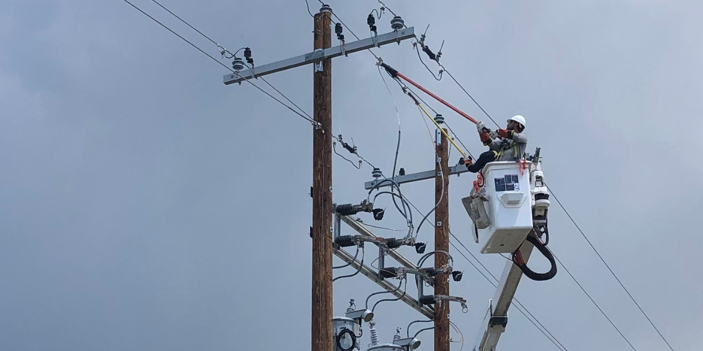 Lineman in a bucket truck at the top of a power pole
